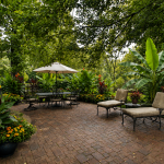 Resort-style summer patio with Northern Wonder banana plants, Cleopatra canna, hibiscus, and cozy wicker seating